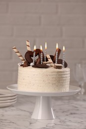 Delicious cake decorated with sweets and burning candles on white marble table