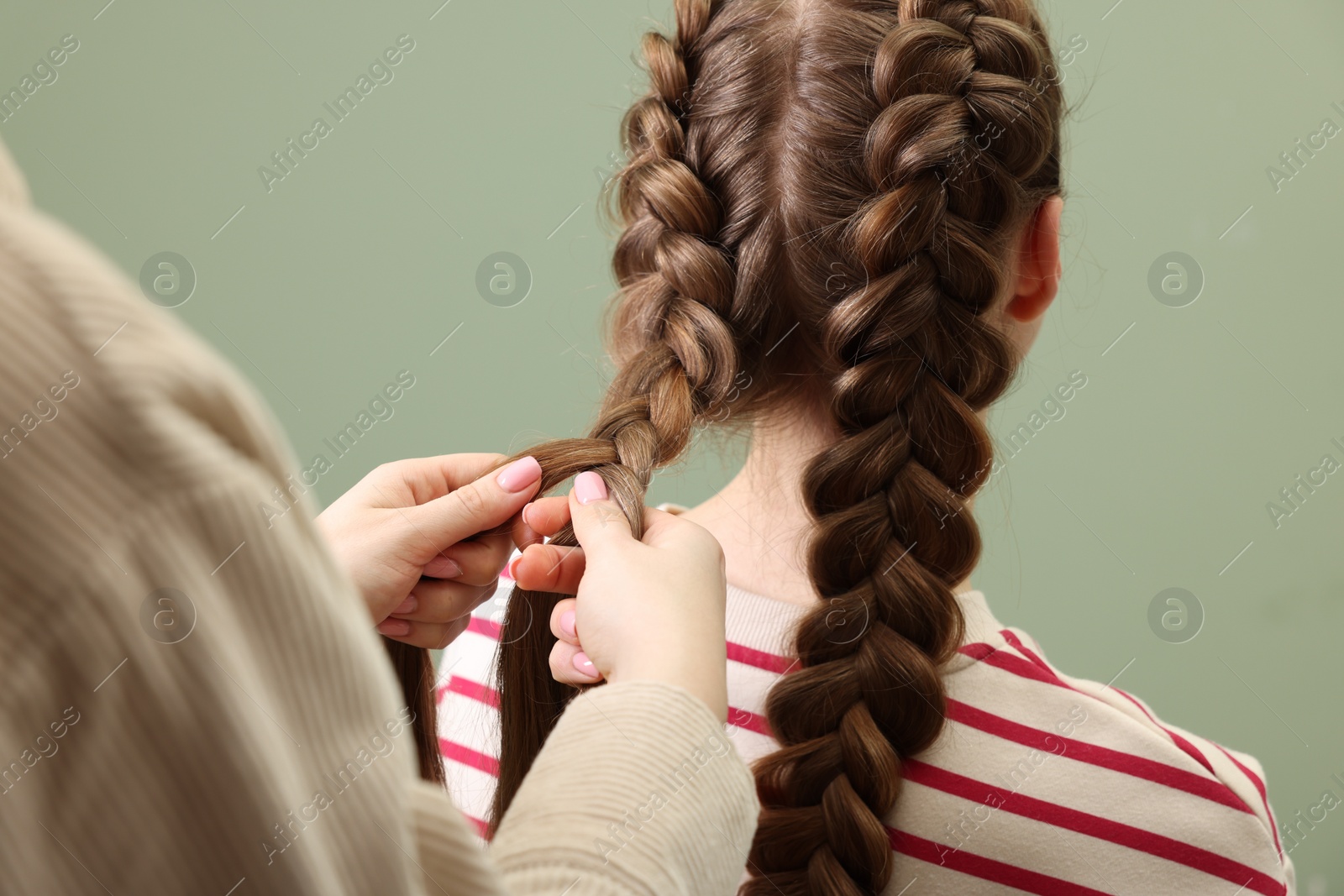 Photo of Professional stylist braiding woman's hair on olive background, closeup