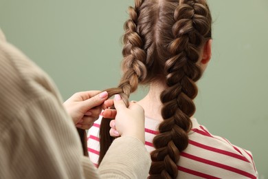 Photo of Professional stylist braiding woman's hair on olive background, closeup