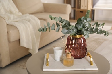 Photo of Bunch of eucalyptus branches and oil diffuser on table in living room. Interior design