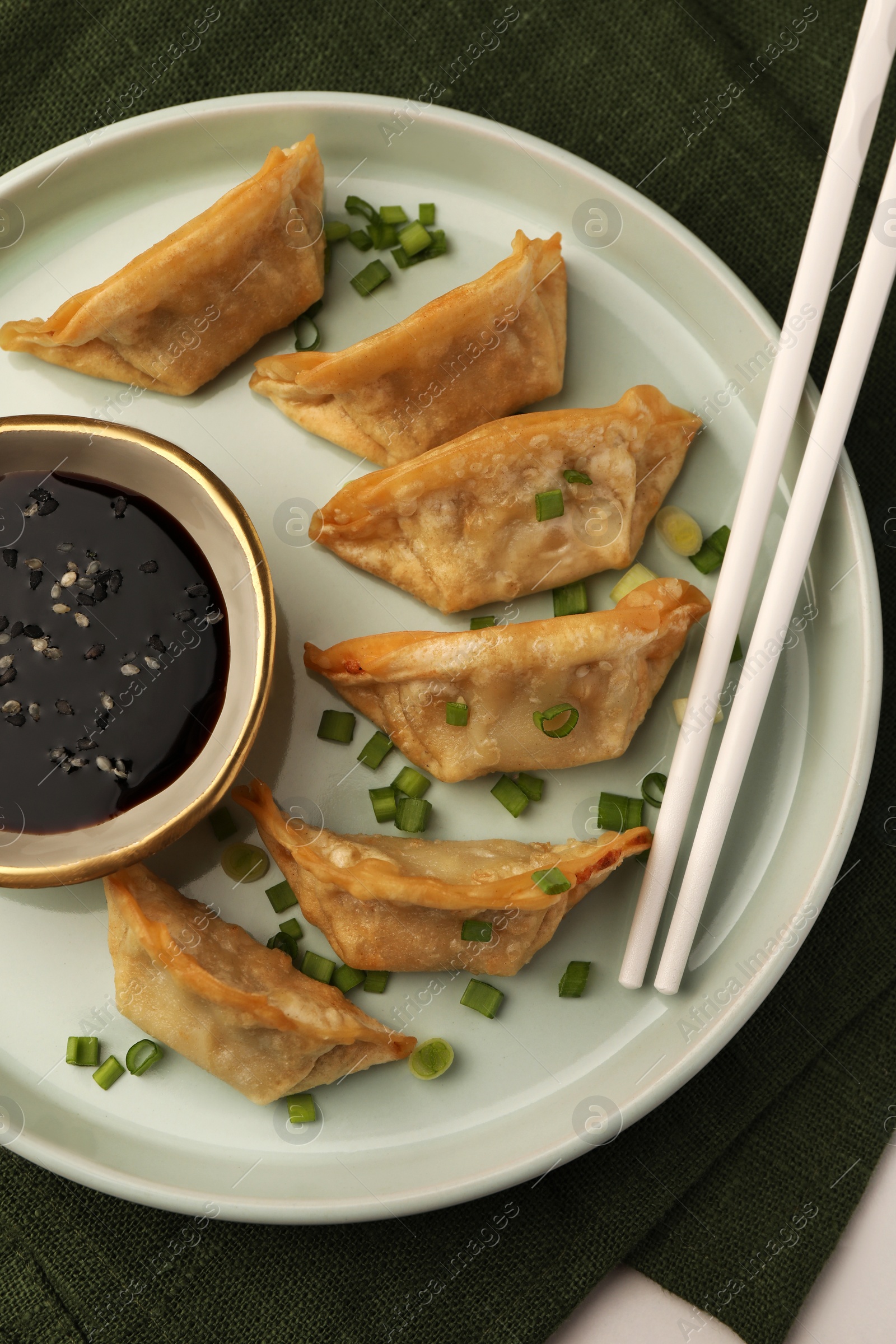 Photo of Delicious gyoza (asian dumplings) with soy sauce, green onions and chopsticks on table, top view