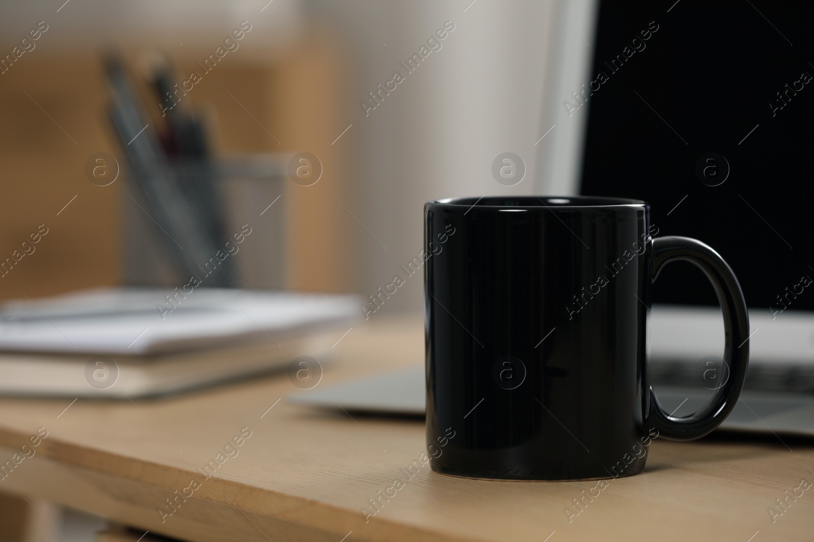 Photo of Black ceramic mug and laptop on wooden table at workplace. Space for text