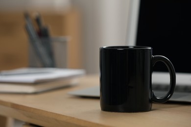 Black ceramic mug and laptop on wooden table at workplace. Space for text