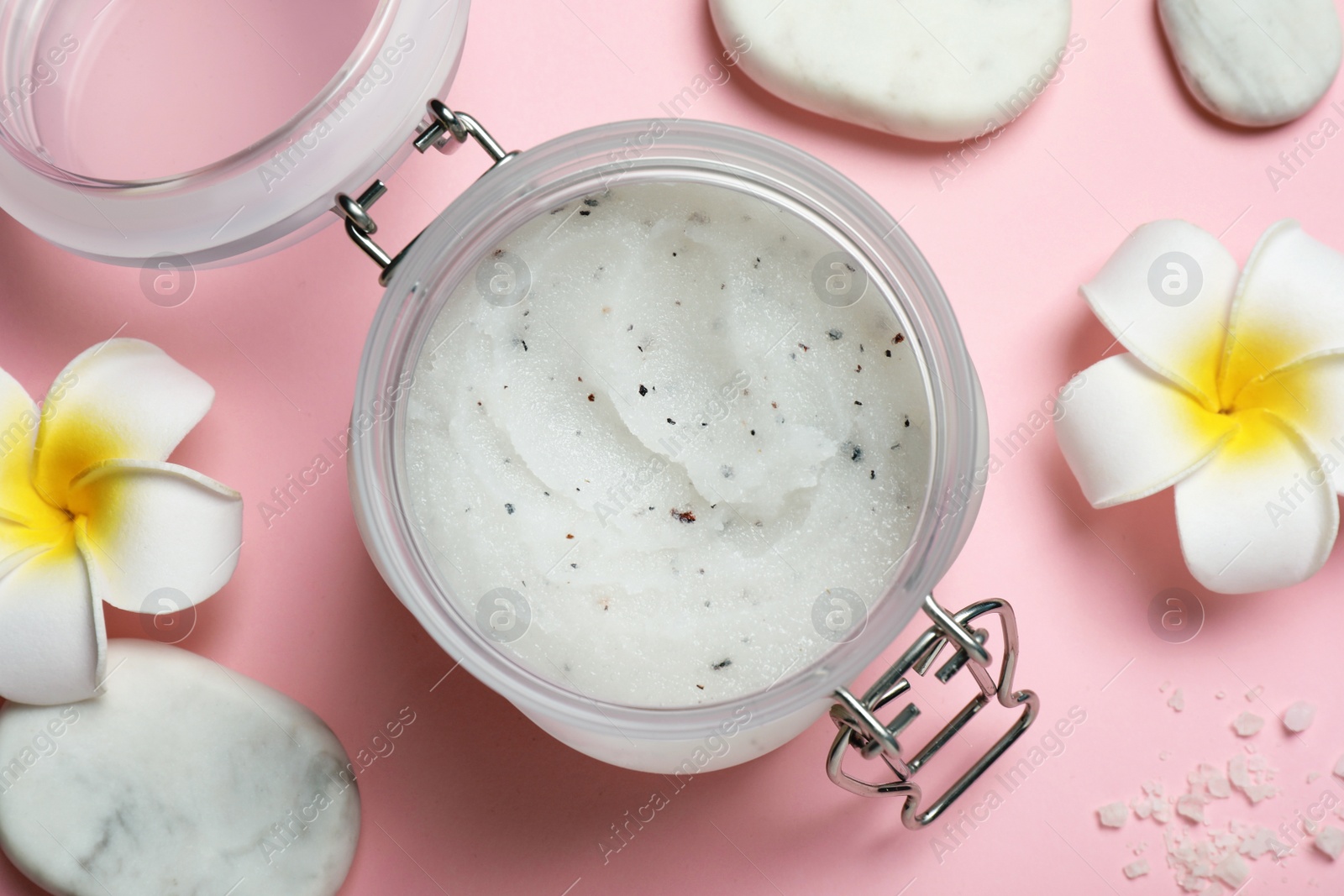 Photo of Body scrub, spa stones and plumeria flowers on pink background