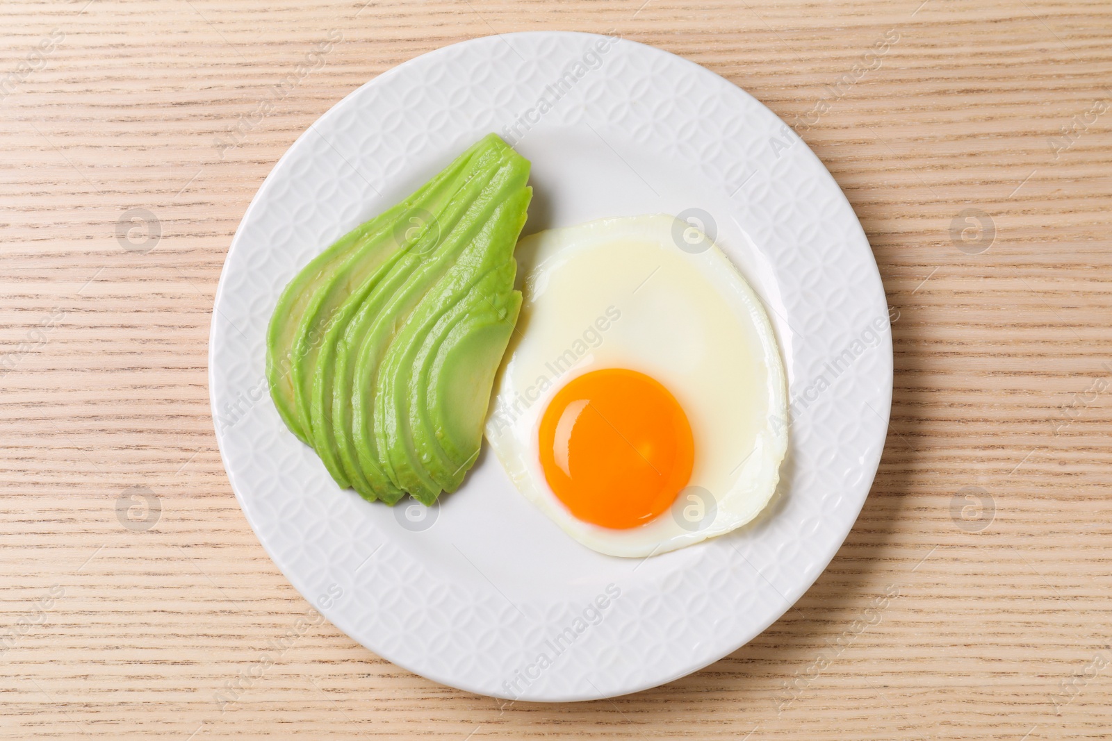 Photo of Plate of fried egg and avocado on wooden table, top view. Healthy breakfast