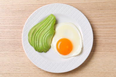 Photo of Plate of fried egg and avocado on wooden table, top view. Healthy breakfast