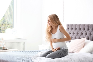 Photo of Young pregnant woman suffering from pain in bedroom. Gynecology concept