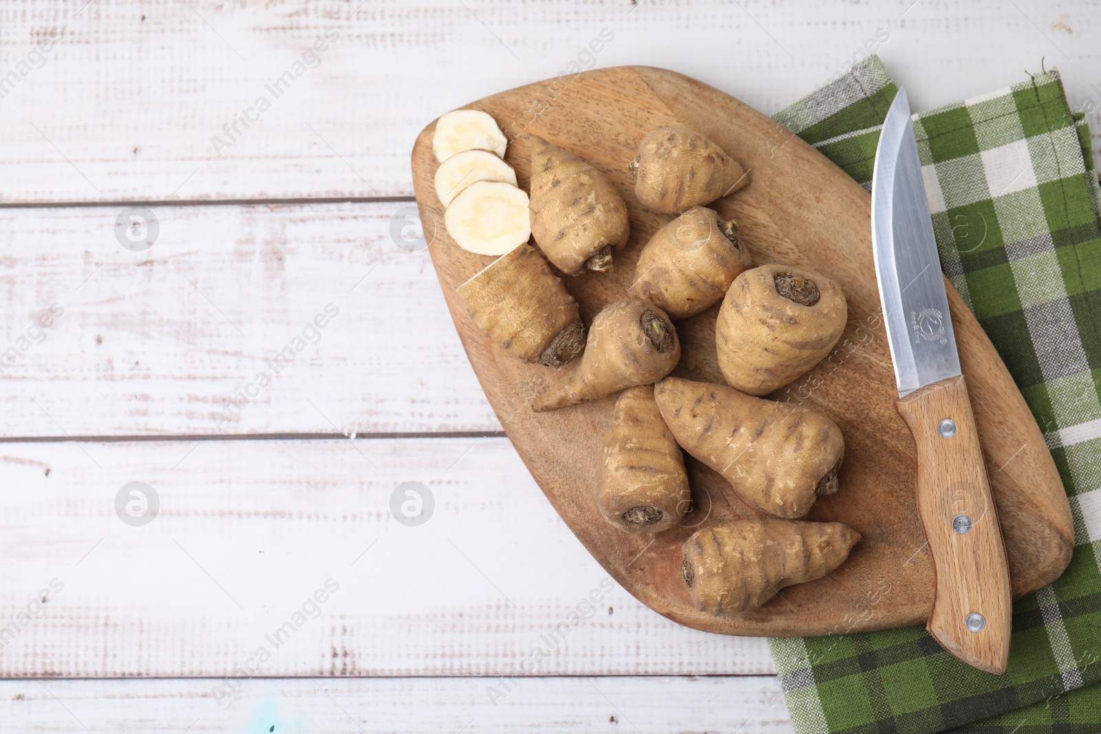 Photo of Turnip rooted chervil tubers and knife on light wooden table, top view. Space for text