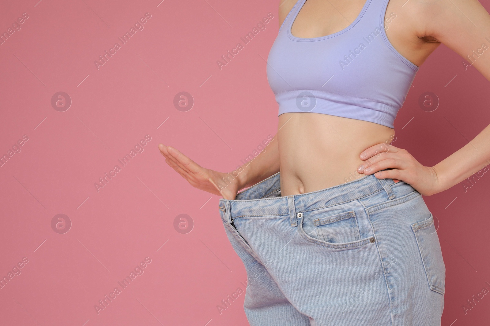 Photo of Woman in big jeans showing her slim body on pink background, closeup. Space for text