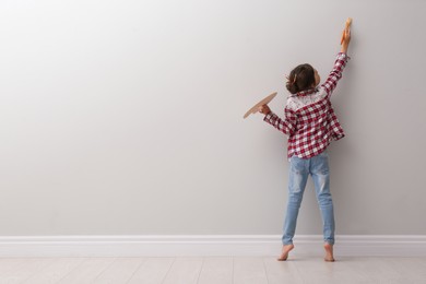 Photo of Little girl painting on light grey wall indoors, back view. Space for text