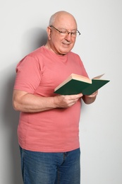 Portrait of senior man with glasses reading book on light background
