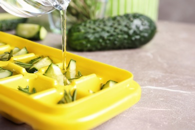 Photo of Pouring water into ice cube tray with cucumber and rosemary on table, closeup. Space for text