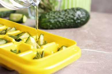 Pouring water into ice cube tray with cucumber and rosemary on table, closeup. Space for text