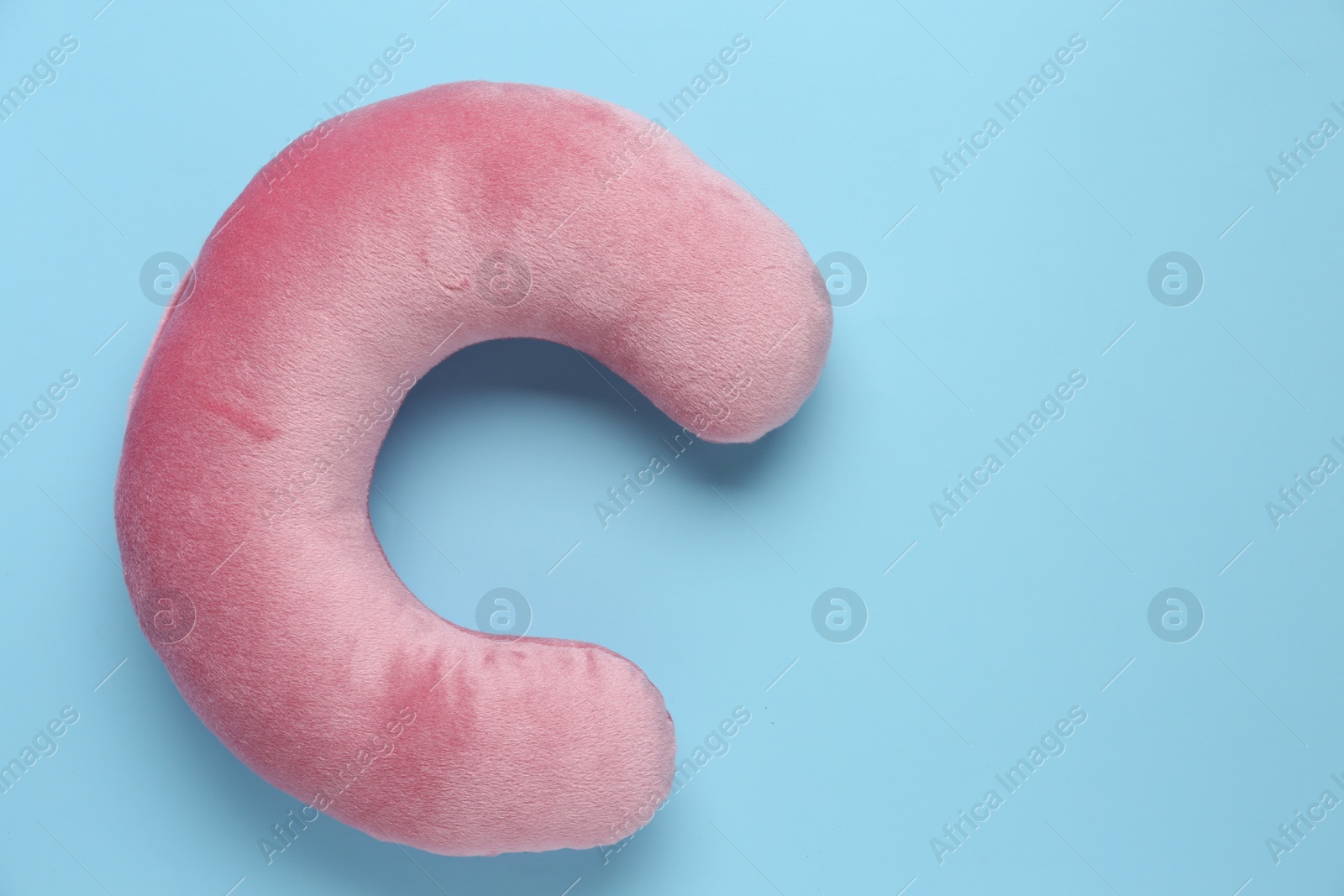 Photo of Pink travel pillow and sunglasses on light blue background, top view. Space for text