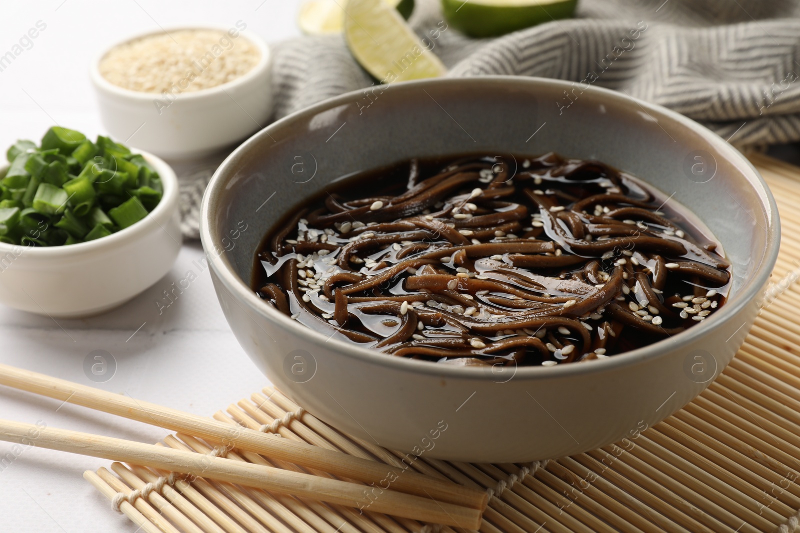 Photo of Tasty buckwheat noodles (soba) with sauce in bowl and chopsticks on white table, closeup