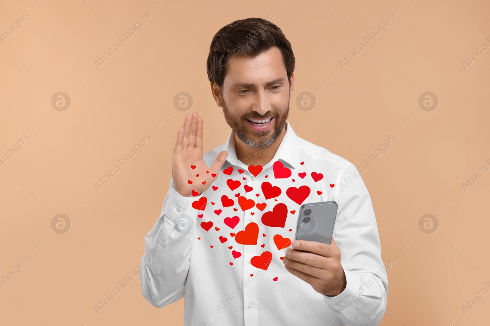 Image of Long distance love. Man video chatting with sweetheart via smartphone on dark beige background. Hearts flying out of device