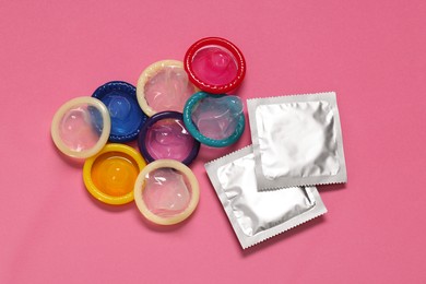Unpacked condoms and packages on pink background, flat lay. Safe sex