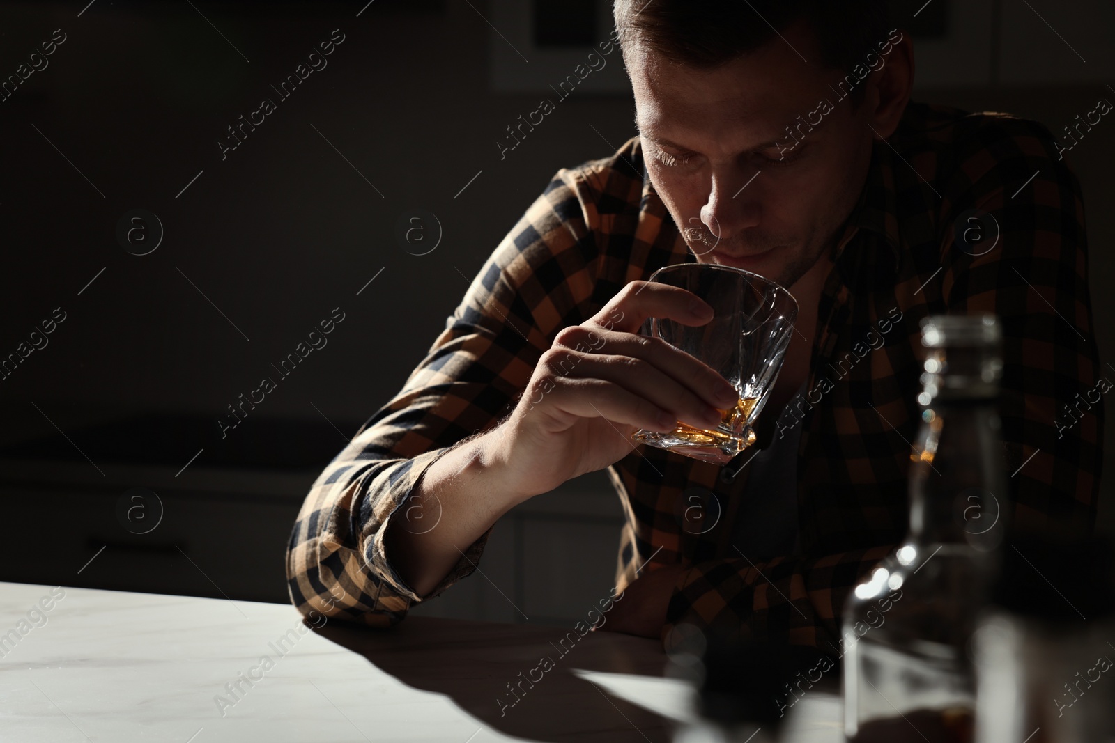 Photo of Addicted man drinking alcohol at table in kitchen