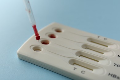 Dropping blood sample onto disposable multi-infection express test cassette with pipette on light blue background, closeup