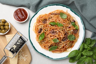 Delicious pasta with anchovies, tomato sauce, cheese and basil on light grey table, flat lay