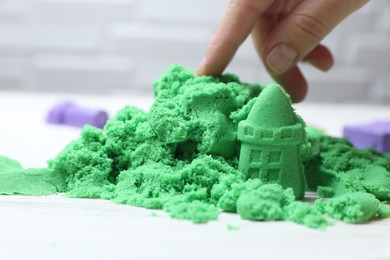 Woman playing with green kinetic sand at white table, closeup