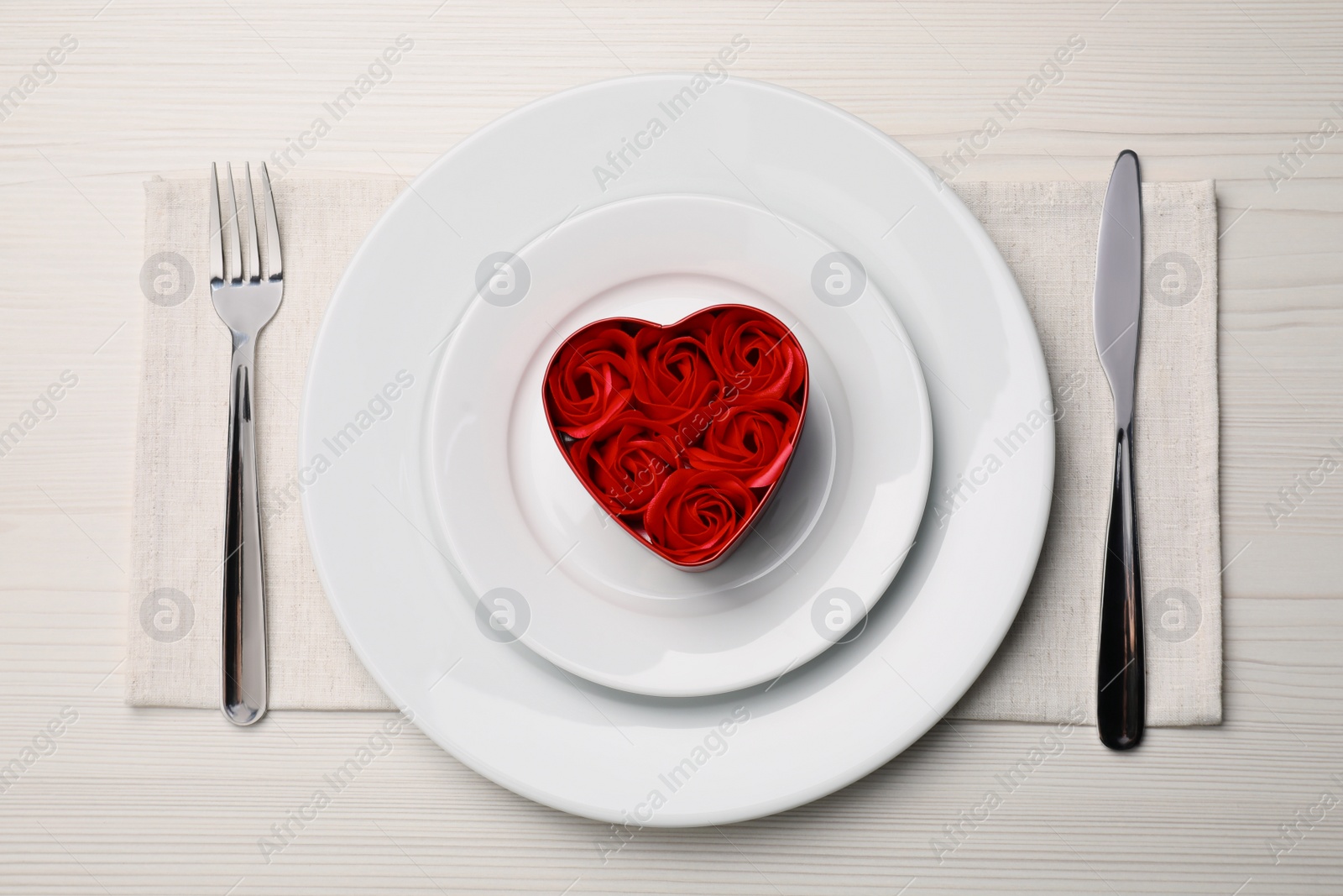 Photo of Beautiful table setting. Dishware and decorative heart shaped box with roses for romantic dinner on white wooden table, flat lay