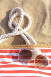 Photo of Stylish sunglasses and beach bag on sand
