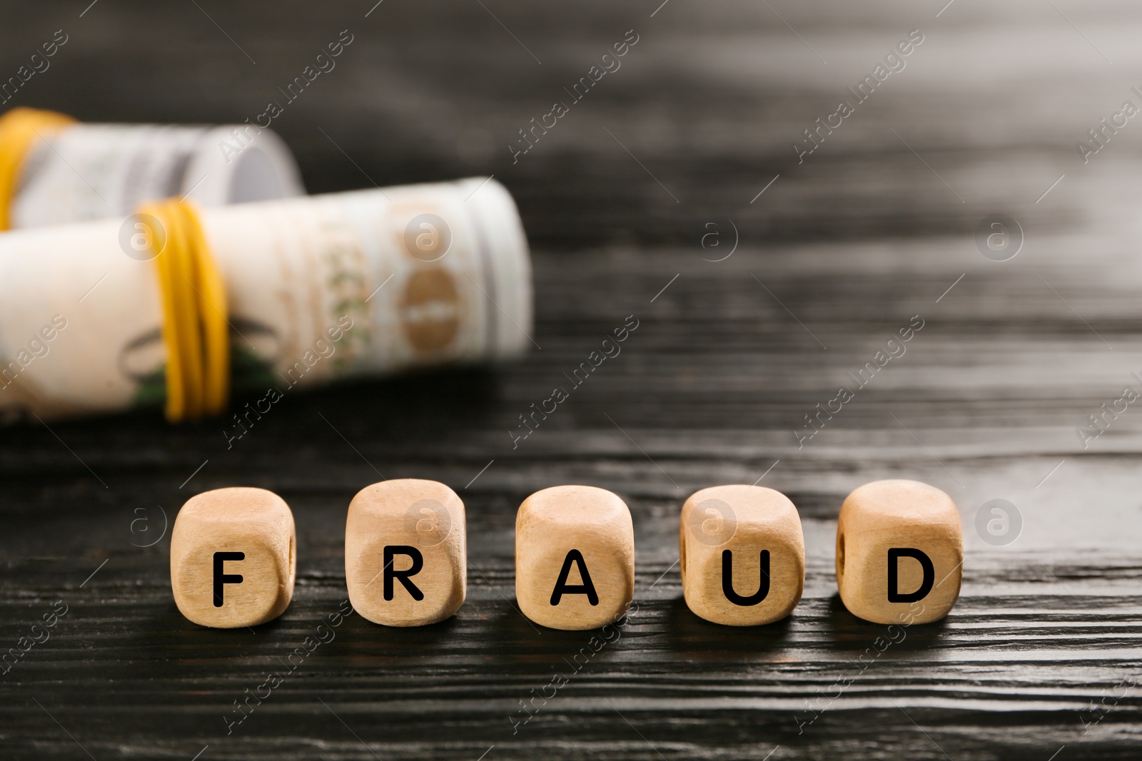 Photo of Word Fraud of cubes with letters near rolled dollar banknotes on black wooden table. Space for text