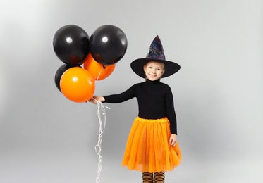 Photo of Cute little girl with balloons wearing Halloween costume on grey background