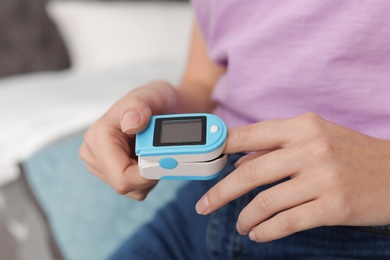 Photo of Young woman checking pulse with digital medical device indoors, closeup