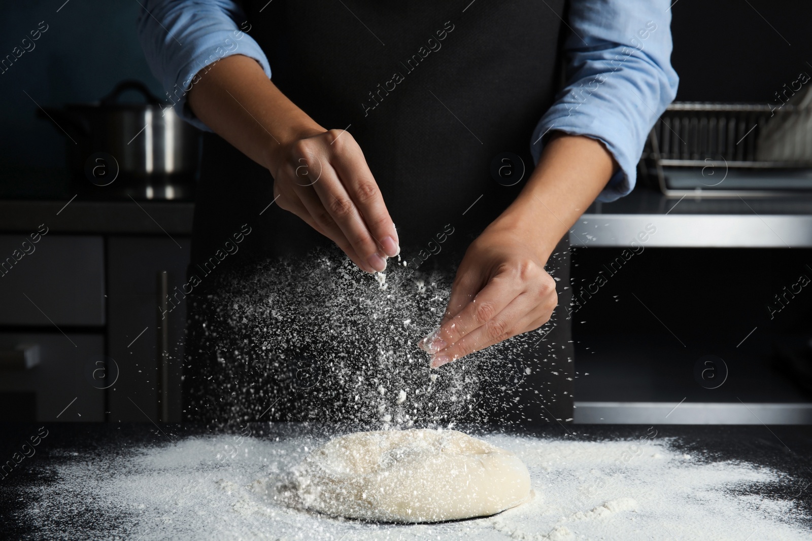 Image of Woman sprinkling flour over dough on table in kitchen, closeup