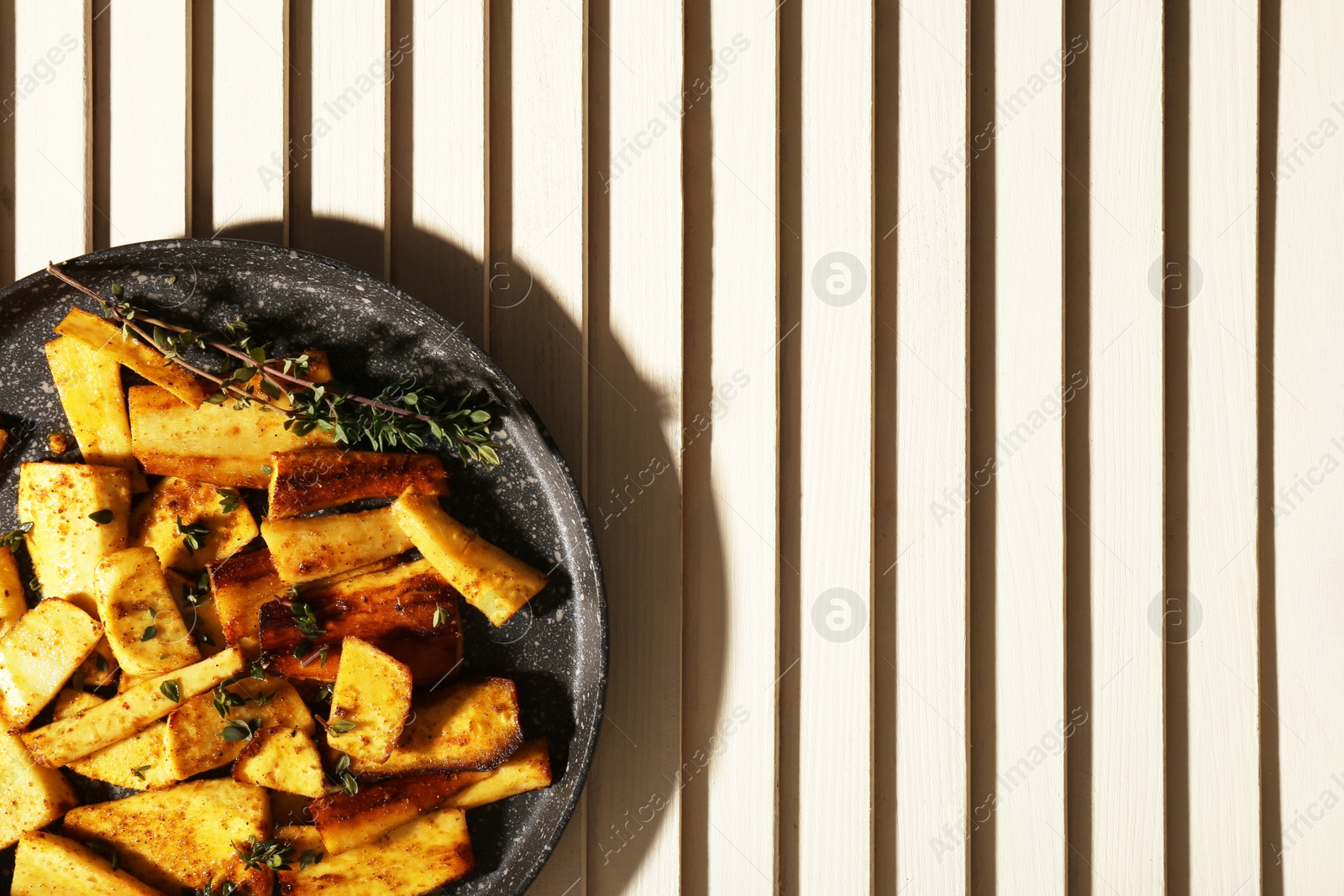 Photo of Delicious parsnips with thyme in frying pan on white wooden table, top view. Space for text