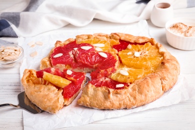 Photo of Tasty galette with citrus fruits and almond flakes on white table