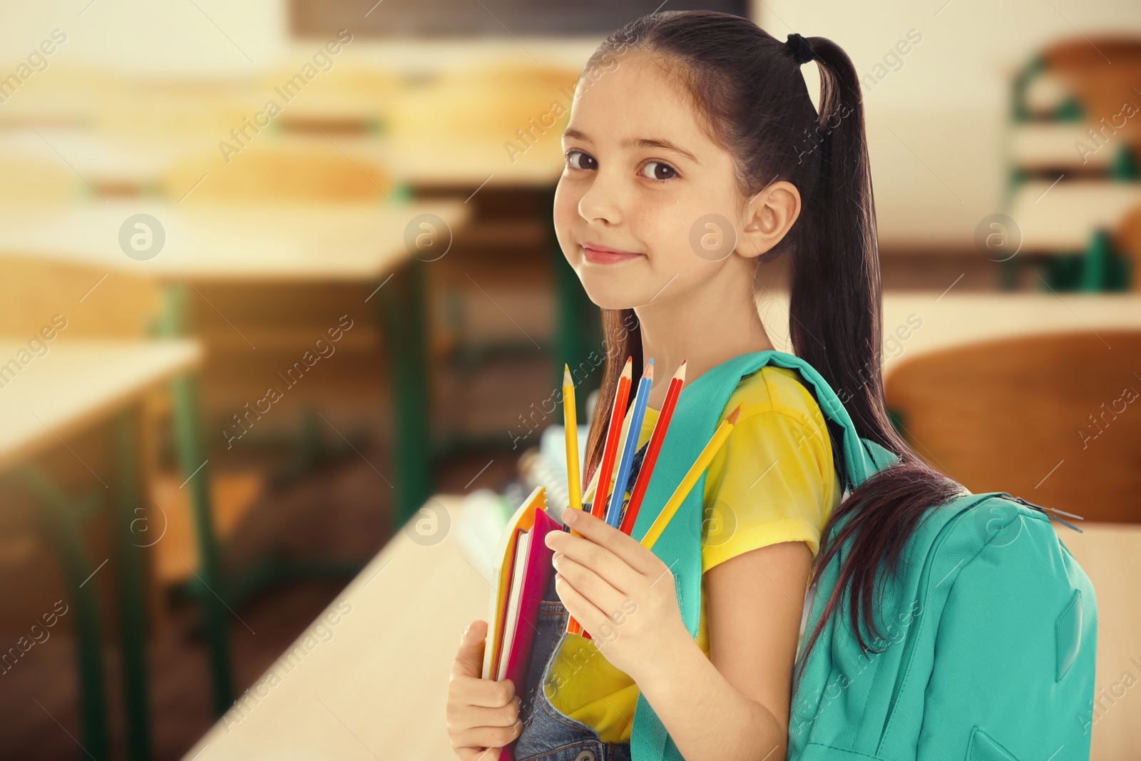 Image of Little girl with school stationery in empty classroom