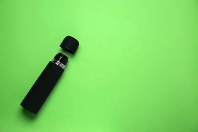 Black thermos and cup on green background, flat lay. Space for text