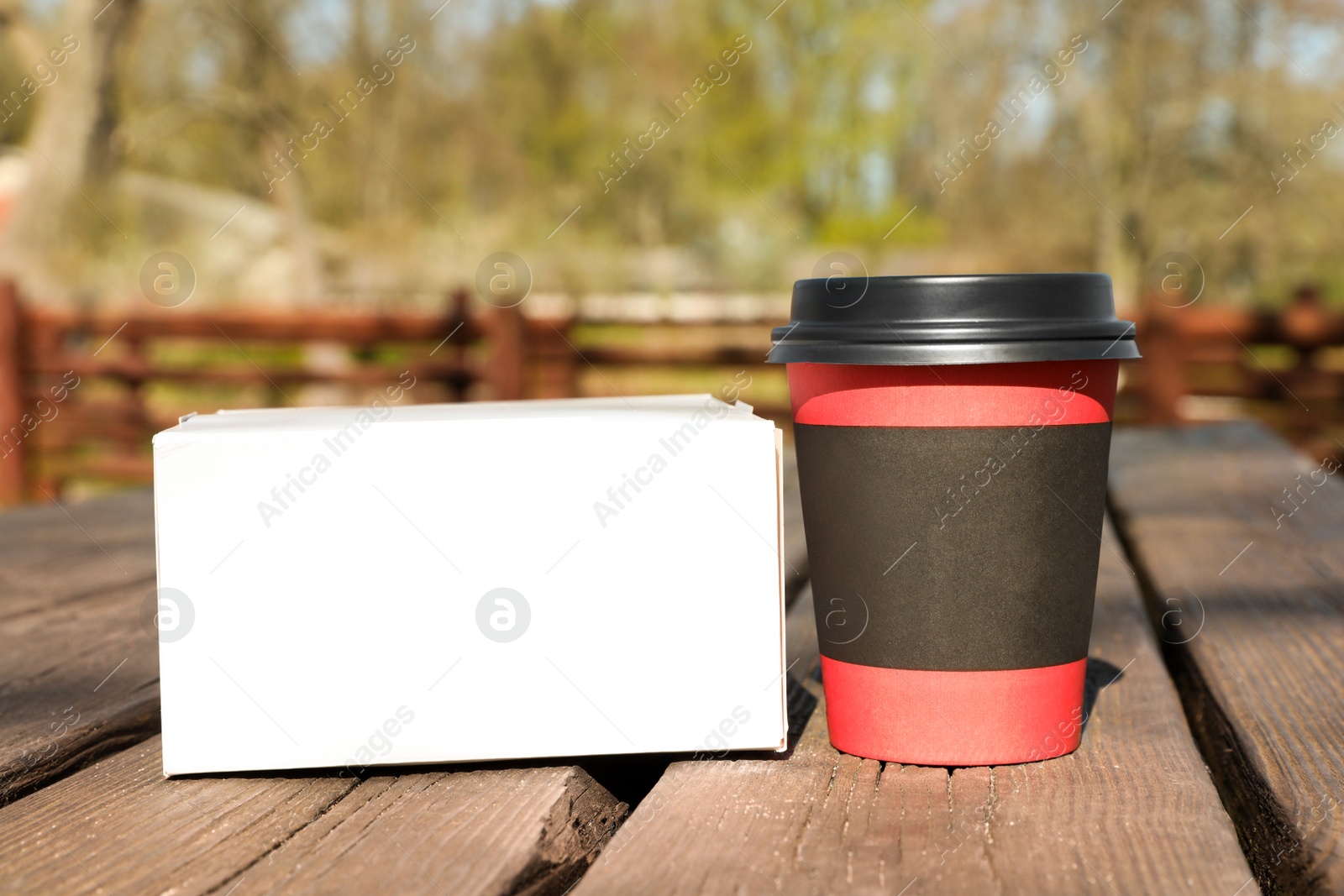 Photo of Hot coffee in takeaway cup and box with dessert on wooden table outdoors