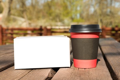 Photo of Hot coffee in takeaway cup and box with dessert on wooden table outdoors