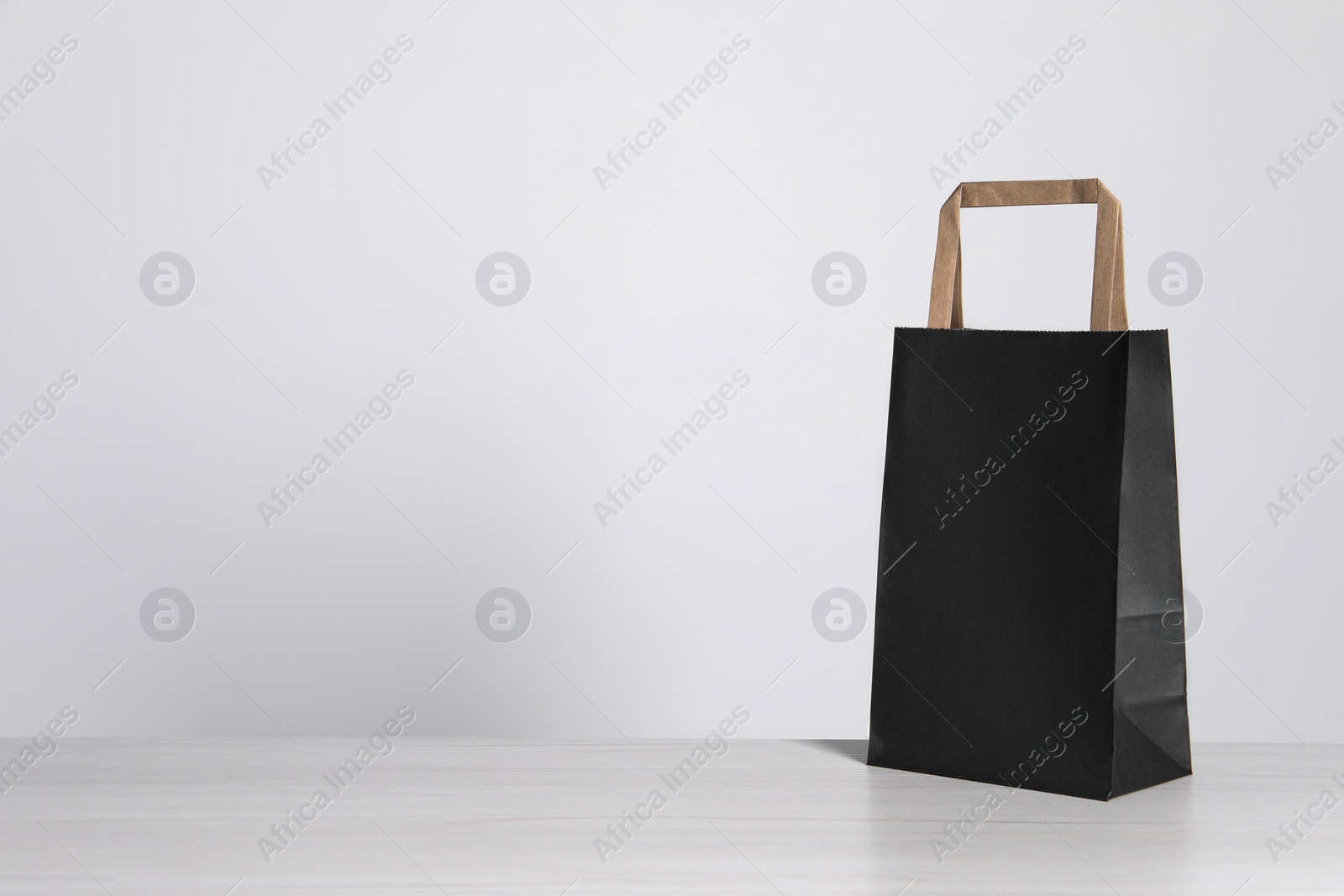 Photo of Black paper bag on white wooden table, space for text