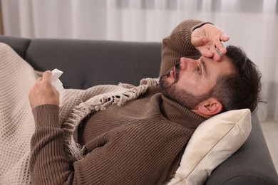 Photo of Sick man with tissue lying on sofa at home. Cold symptoms