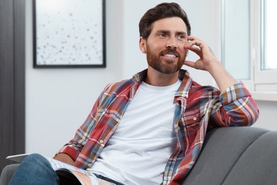 Photo of Smiling bearded man looking away on sofa indoors