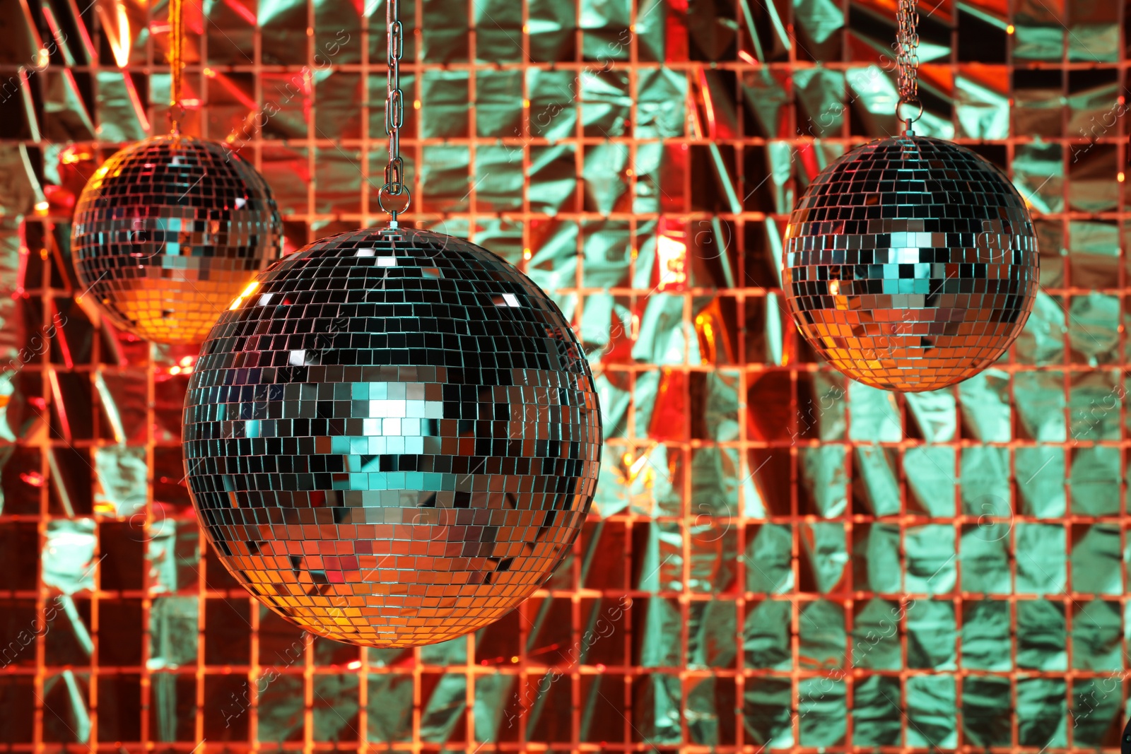 Photo of Shiny disco balls against foil party curtain under color lights