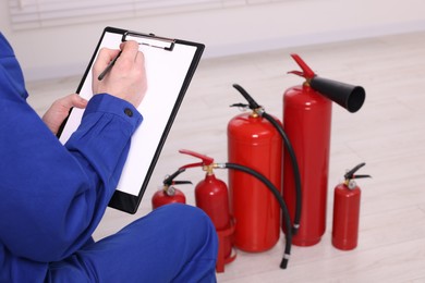 Photo of Man with clipboard checking fire extinguishers indoors, closeup