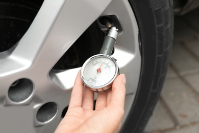 Photo of Woman checking car tire pressure with air gauge, closeup