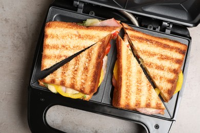 Photo of Modern grill maker with tasty sandwiches on light grey table, top view