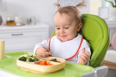 Cute little baby eating food in high chair at home