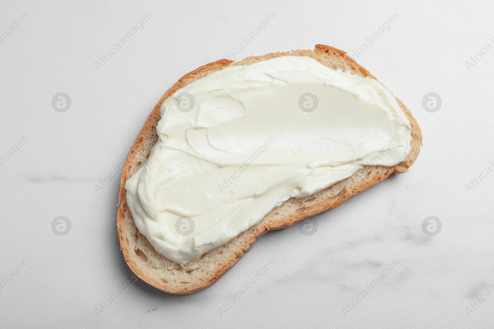 Photo of Slice of bread with tasty cream cheese on white marble table, top view