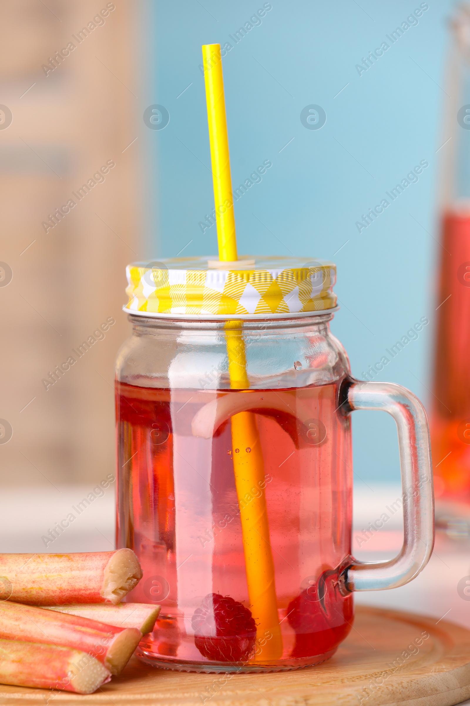 Photo of Mason jar of tasty rhubarb cocktail with raspberry and stalks on table