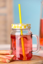 Mason jar of tasty rhubarb cocktail with raspberry and stalks on table