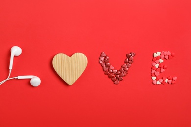 Photo of Word Love made with sprinkles, wooden heart and modern earphones on red background, flat lay. Listening music songs