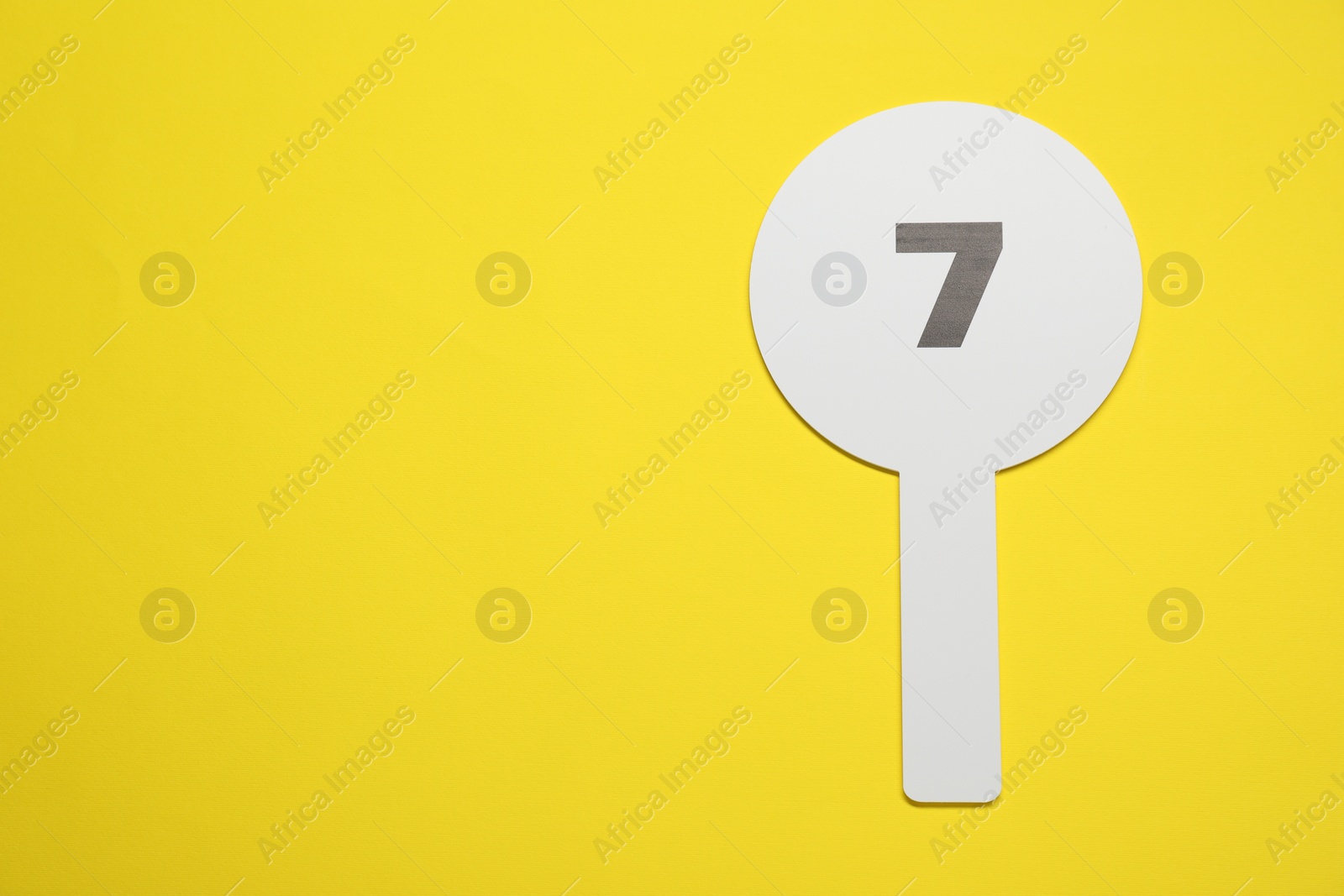Photo of Auction paddle with number 7 on yellow background, top view. Space for text